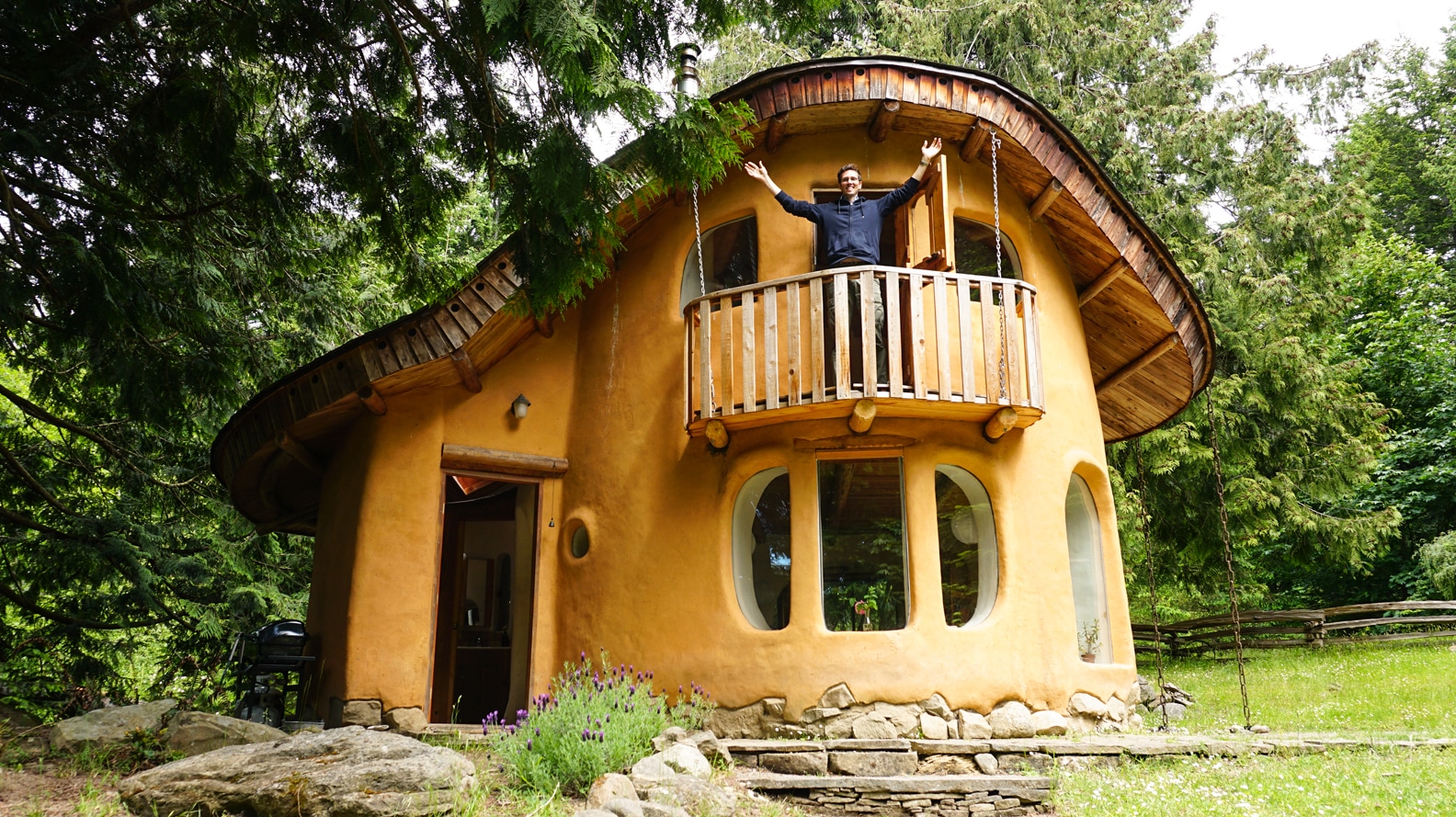 Man With Arms Outstretched Outside of Cob House