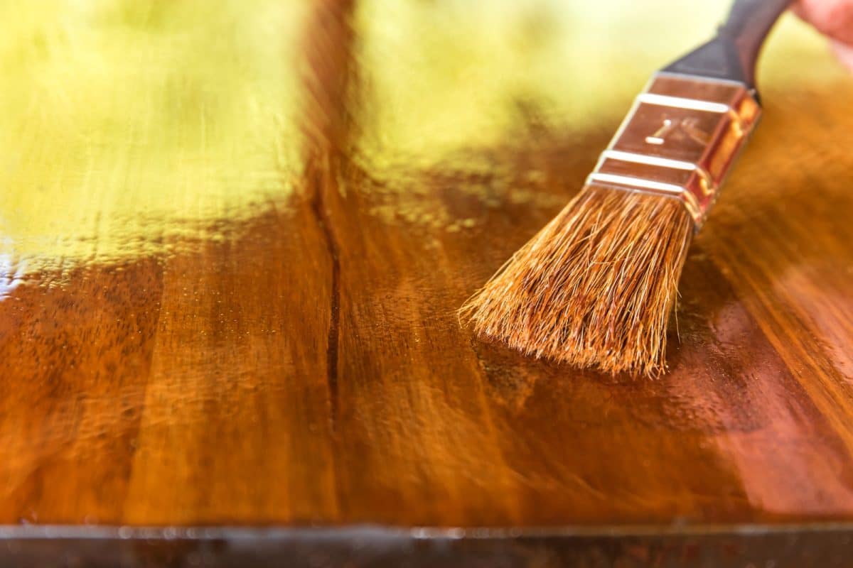 Applying protective oil on a wooden furniture. Varnishing the table top of acacia wood. Close-up view of a paintbrush. Housework. paint brush applying wood oils on a table